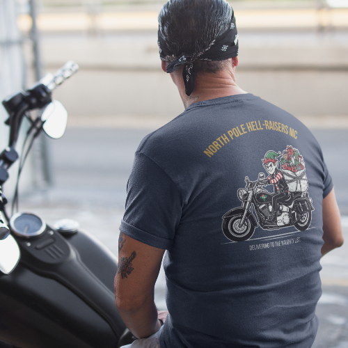 A man wearing a dark gray t-shirt with a large graphic print on the back, sitting on a black motorcycle in an outdoor setting.